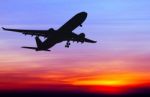 Silhouetted Commercial Airplane Flying At Sunset Stock Photo