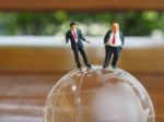 Miniature Businessman Stand On Globe Of Glass With Wooden Backgr Stock Photo