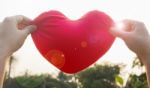 Hands Hold Or Raise Big Red Heart To Sky With Lens Flare And Sun Stock Photo