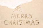 Merry Christmas Inscription On Wet Yellow Beach Sand Stock Photo