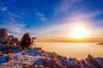 Professional Photographer Takes Photos With Camera On Tripod On Rocky Peak At Sunset Stock Photo