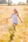 Happy Young Blonde Girl In White Dress With Straw Hat Running Th Stock Photo