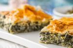 Greek Pie Spanakopita On The White Plate With Blurred Accessorizes Horizontal Stock Photo