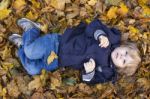 Toddler Blond Boy With Blue Eyes Lays On Bed Of Autumn Fallen Le Stock Photo