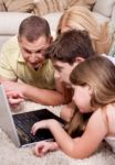 Domestic Family Of Four Lying And Working With Laptop Stock Photo