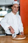 Experienced Chef Cutting Pizza With Cutter Stock Photo