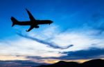 Silhouetted Commercial Airplane Flying At Sunset Stock Photo