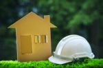 Paper Home Out Line With Safety Helmet On Green Grass Field Wtih Stock Photo