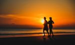 Young Couple: Man And Woman Run Together On A Sunset On Lake Coa Stock Photo