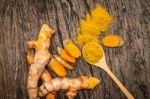 Turmeric Powder In Spoon And Roots On Wooden Plate Stock Photo