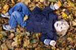 Toddler Blond Boy With Blue Eyes Lays On Bed Of Autumn Fallen Le Stock Photo