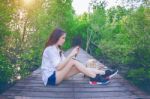 Girl Sitting Alone And Hand Holding Camera On A The Wooden Bridg Stock Photo