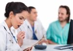 Young Asian Doctor Thinking With The Pen, Others Blurred Behind Stock Photo