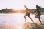 A Couple Is Running On Beach While The Sun Is Set Stock Photo