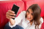 Young Woman Making Face While Taking Selfie On Sofa Stock Photo