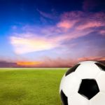 Soccer Ball With Green Grass Field Against Sunset Sky Stock Photo