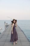 Portrait Of Beautiful Young Woman Wearing Wide Straw Hat And Long Dress Standing With Happiness Emotion On Piers At Sea Beach Stock Photo