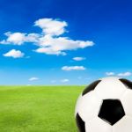 Soccer Ball With Green Grass Field Against Blue Sky Stock Photo