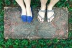 Top View Feet Of Male And Female Couple Lover Standing On Stone Floor Among Little Green Grass Garden. Hipster Style Stock Photo