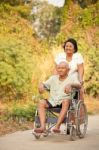 Senior Woman Pushing Her Disabled Hasband On Wheelchair Stock Photo