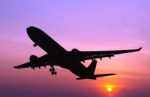 Silhouetted Commercial Airplane Flying At Sunset Stock Photo