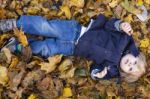 Toddler Blond Boy With Blue Eyes Lays On Bed Of Autumn Fallen Le Stock Photo