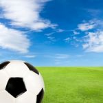 Soccer Ball With Green Grass Field Against Blue Sky Stock Photo