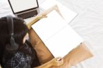 Asian Girl Sitting On Bed Reading Blank Book Listening To Music Stock Photo