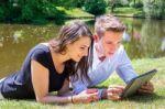 Young Man And Woman Lying At Water Reading Ipad Stock Photo