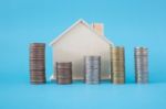 Stack Of Coins And Wooden House Symbol On Blue Soft Background Stock Photo