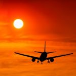 Silhouetted Commercial Airplane Flying At Sunset Stock Photo