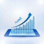 Businessman Flying Toward The Top Of Business Graph On Mobile Stock Photo