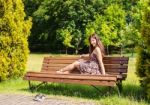 Young Beautiful Brunette Sitting On A Bench In A City Park Stock Photo