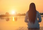 Silhouette Of Relaxing Young Woman On Wooden Pier At The Lake In Sunset Stock Photo