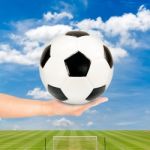 Hand Holding Soccer Ball With Soccer Field And Blue Sky Stock Photo