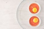 Raw Eggs With Tomatoes In The Ramekins On The White  Wooden Table Top View Stock Photo