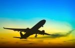 Silhouetted Commercial Airplane Flying At Sunset Stock Photo