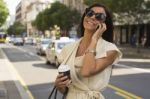 Smiling Young Woman With Coffee Laughs Into Phone Stock Photo