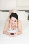 Lady Lying On Bed With Cellphone Stock Photo