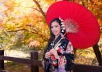 Asian Woman Wearing Traditional Japanese Kimono With Red Umbrella In Autumn Stock Photo