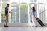 Woman With Luggage Waving To Boyfriend At Airport Stock Photo