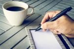 Man Hand With Pen Writing On Notebook. Coffee And Notebook On Wooden Table Stock Photo