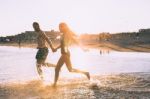 A Couple Is Running On Beach While The Sun Is Set Stock Photo