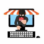 Man Wearing Balaclava And Holding Credit Card While Using Laptop At Desk Stock Photo