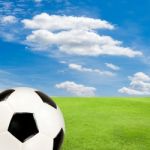 Soccer Ball With Green Grass Field Against Blue Sky Stock Photo