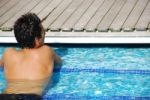 Young Man Relaxing At The Edge Of The Swimming Pool Stock Photo