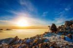 Professional Photographer Takes Photos With Camera On Tripod On Rocky Peak At Sunset Stock Photo