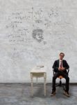 Man Sitting On Desk And Physic Formula On Wall Stock Photo