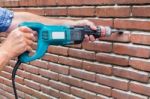 Arms Holding Drilling Machine Against Brick Wall Stock Photo