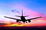 Silhouetted Commercial Airplane Flying At Sunset Stock Photo